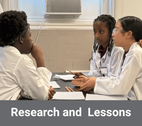 Middle school girls in lab coats discussing science with databots on the table in front of them.